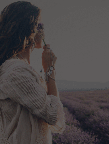 Woman smelling lavender in a field, representing natural wellness and holistic lifestyle.